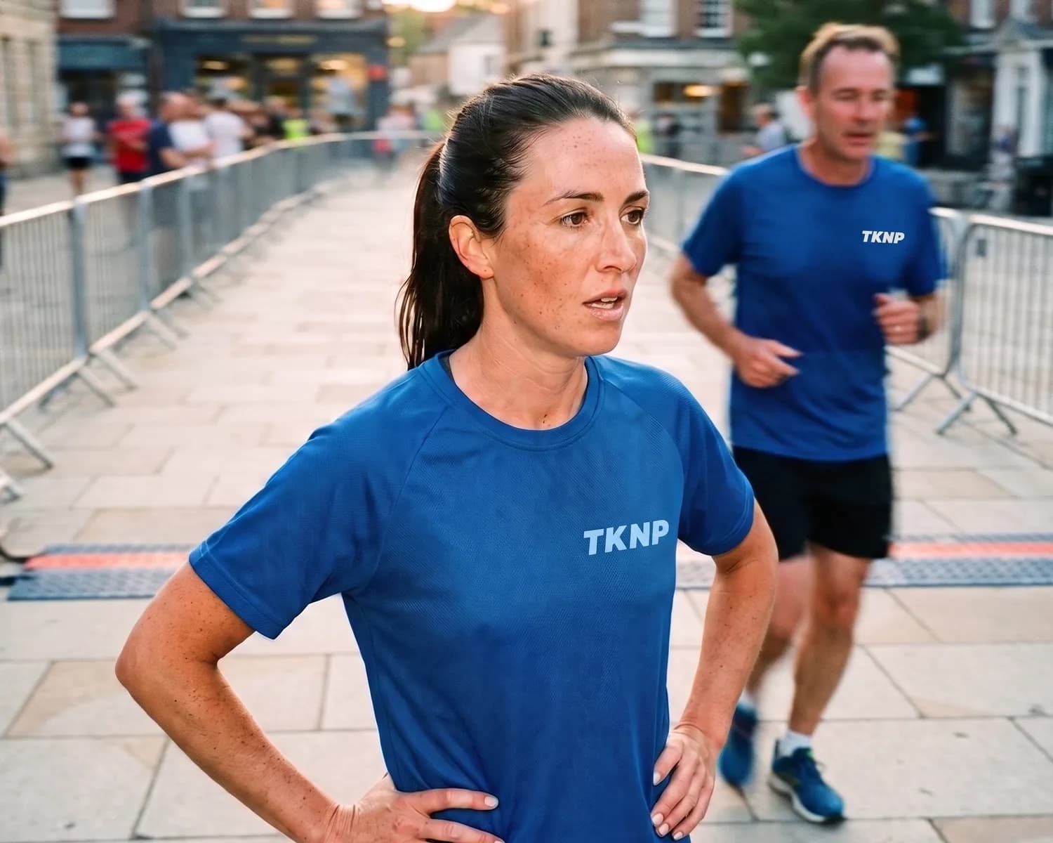 T-shirt technique personnalisé bleu roi : une coureuse porte un t-shirt de sport au petit logo TKNP bleu clair côté cœur, la matière choisie pour l'effort plutôt que le coton.